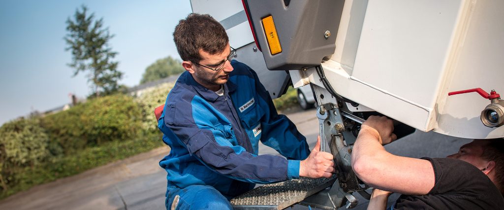 Ein Servicetechniker repariert ein Kommunalfahrzeug mit Hilfe eines Schraubenschlüssels.